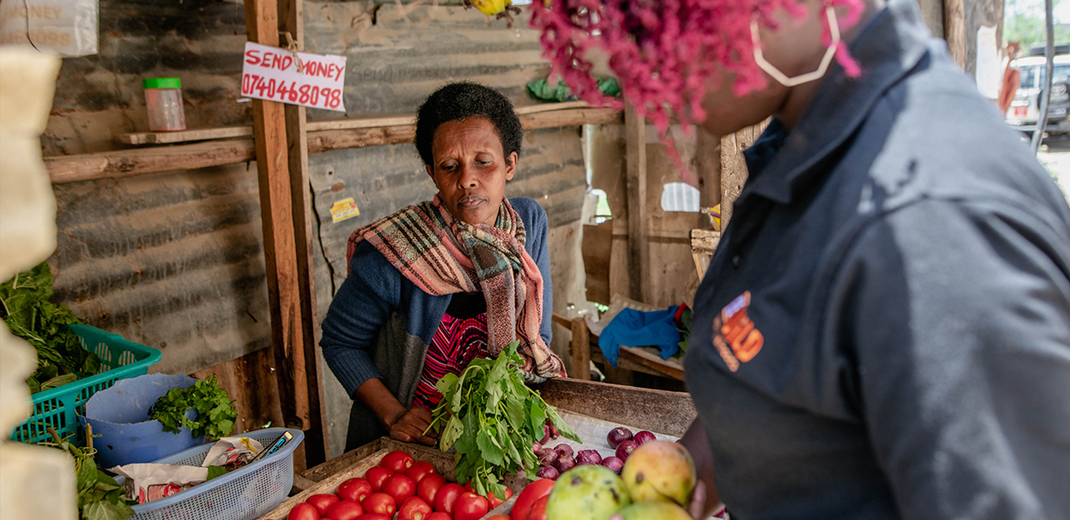 A Congolese produce vendor looks as Mercy Corps staff select fruit.